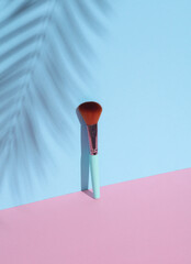 Wall Mural - Makeup brush on a pink blue background with palm leaf shadow. Beauty concept. Creative layout, minimalism