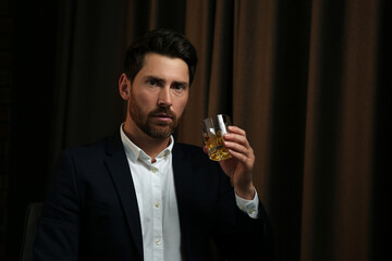 Wall Mural - Man in suit holding glass of whiskey with ice cubes on brown background