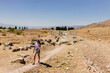 A young woman in a striped top and blue denim shorts walks along a picturesque road between the ruins of an ancient city. Journey to the old city. Hierapolis, Pamukkale, Türkiye - July 29, 2023