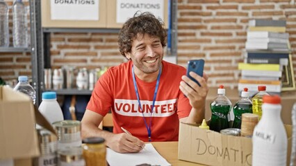 Canvas Print - Young hispanic man volunteer writing on clipboard having video call at charity center