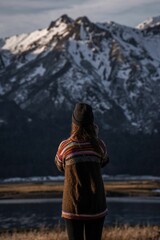 Wall Mural - Vertical shot of a young woman standing on the background of the snowy mountain in the highland