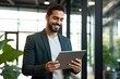 © Adriana - Happy young business man executive holding pad computer at work. Male professional employee using digital tablet fintech device standing in office checking financial online market data