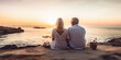 © SnowElf - Senior couple sitting on the sandy beach and looking at the sea sunset. Meet old age at the seaside, a tourism concept.