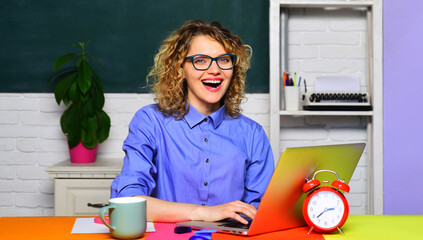 Wall Mural - Smiling university student girl preparing for test or exam using laptop. High school. Female teacher in glasses working with notebook computer in classroom. Teacher job. Education, learning, teaching.