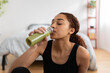 © Xavier Lorenzo - Young latin woman drinking detox green juice after workout routine at home. Healthy lifestyle concept