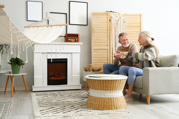 Mature couple drinking tea near fireplace at home