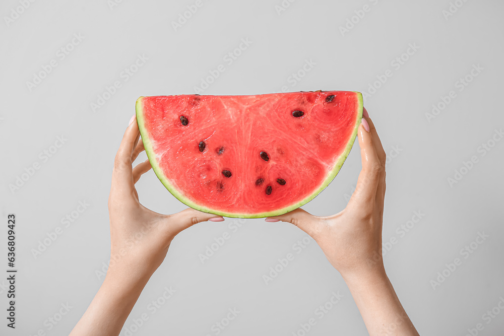 Female hands with piece of ripe watermelon on light grey background