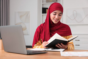 Poster - Muslim woman studying near laptop at wooden table in room