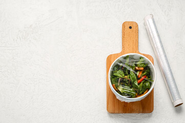 Wall Mural - Bowl of fresh salad covered with plastic food wrap on light background