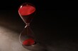 Hourglass with red flowing sand on grey table. Space for text