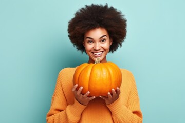 Attractive happy young black woman holding a pumpkin looking at the camera of cyan background