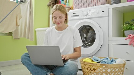 Wall Mural - Young blonde woman using laptop smiling at laundry room