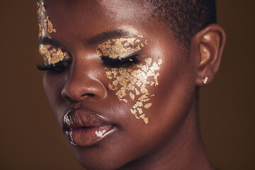 Gold, creative and black woman with makeup for beauty aesthetics isolated in a studio brown background eyes closed. Art, luxury and face of African person with cosmetic glamour or design for skincare