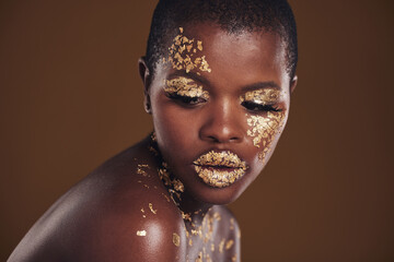 Art, studio and black woman with gold makeup on brown background, glitter paint facial and cosmetics. Shine, glow and face of African model for beauty, fashion or aesthetic freedom in luxury skincare