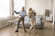 © fizkes - Cheerful active retired elder dancing to disco music in spacious living room, having fun, enjoying sportive hobby, home party, celebrating anniversary, family special date