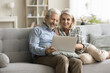 © fizkes - Positive retired senior husband and wife using online application on laptop, relaxing on home couch together, enjoying wireless Internet communication, family video call talk