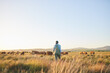 © Charlize Davids/peopleimages.com - Woman, farmer and walking in countryside, blue sky and grass field with cow and cattle. Female person, back and agriculture outdoor with animals and livestock for farming in nature with mockup space