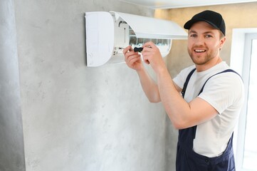 Wall Mural - Smiling young male electrician repair conditioner in client home. Man mechanic or repairman fix filters in air condition device at customer house