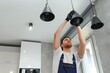 © Serhii - A male electrician changes the light bulbs in the ceiling light. men's household duties. care of electrical appliances at home