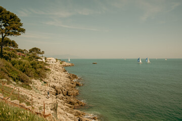 Canvas Print - Yachts sailing by rocky foreshore at Antibes