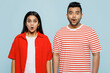 Young shocked surprised astonished couple two friends family Indian man woman wear red casual clothes t-shirt look to each other together isolated on pastel plain light blue cyan color backgroundised.