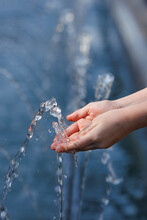 Close-up Hands Of A Little Girl Catching Clear Blue Water From A Fountain