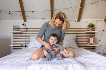 Happy baby boy playing with mom on bed in cozy bedroom