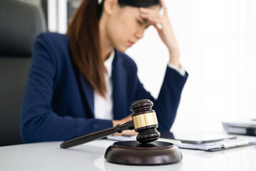 Focus gavel with blur lawyer sitting at her desk with worried and exhausted expression, feeling weight of pressure and stress of making hard decision on verdict with gavel hammer in hand. equity
