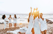 © Prostock-studio - Carefree ladies bride team toasting wine glasses while having hen party and dancing on the beach at coastline