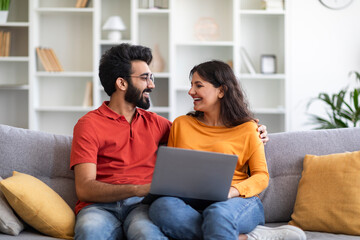 Wall Mural - Portrait Of Happy Indian Couple With Laptop Relaxing On Couch At Home