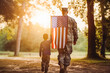 © VisualProduction - Rear view of military man father holding sons hand. Father and son walking together and american flag.