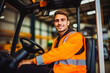 Young forklift driver sitting in vehicle in warehouse. Young male worker in reflective vest.