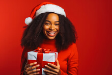 A Black Female Model Dressed As Santa Offers A Gift. Beautiful Black Woman With Santa Hat Holding A Present.
