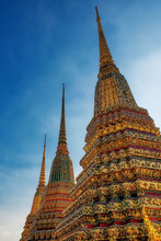 The Spiers Of Three Tall Decorated Buddhist Stupas Against A Clear Blue Sky, Temple Of The Emerald Buddha In Bangkok.