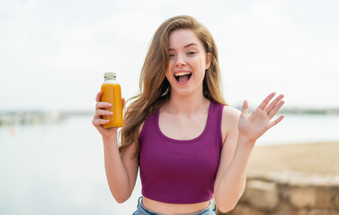 Sticker - Young redhead girl holding an orange juice at outdoors with shocked facial expression