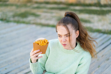 Canvas Print - Young pretty girl holding fried chips at outdoors with sad expression