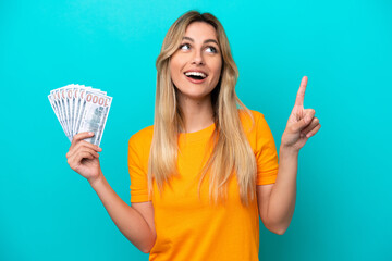 Canvas Print - Young Uruguayan woman taking a lot of money isolated on blue background pointing up a great idea