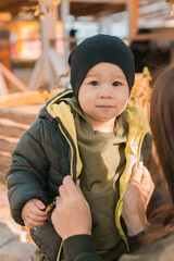 Wall Mural - Mother with her little asian son in autumn park close-up. Woman zips up child jacket. Fall and motherhood concept