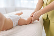 © dikushin - Closeup cropped shot of unrecognizable loving mom helping doing gymnastics exercise massaging to newborn son. Close up hands of professional female masseuse doing exercises with infant baby legs, feet