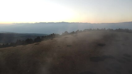 Wall Mural - Drone footage flying over landscape green forest range mountains with misty sunset sky