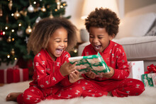 Kids In Matching Pajamas Excitedly Opening One Gift On Christmas Eve , Christmas Eve  