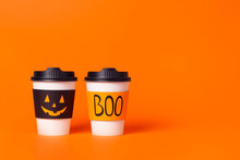 Two Halloween Coffee Cups With Jack-o-lantern Face And Word Boo On Orange Background.