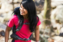An Asian Woman Wearing A Red Shirt Smiles While Hiking With A Backpack In The Woods, Closeup
