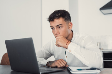 Wall Mural - Thoughtful businessman touching chin, pondering ideas or strategy, sitting at wooden work desk with laptop, freelancer working on online project, student preparing for exam at home
