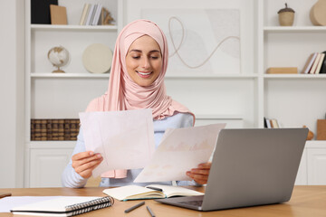 Wall Mural - Muslim woman working near laptop at wooden table in room