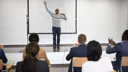 Wall Mural - Positive Hispanic woman standing with microphone on stage in conference room, speaking to businesspeople at seminar. High quality FullHD footage