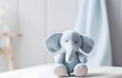 A cute light gray toy elephant is sitting on a wooden table, with a blurred, bright, and cozy nursery room in the background. For Baby shower, card design with copy space. 