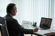 © DragonImages - Middle-aged businessman talking to colleague in online meeting and discussing report