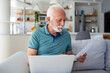 A concerned senior man reads a letter, uncovering business news, an invitation, and bank statement. Highlighting postal correspondence and financial worries in this stock image.
