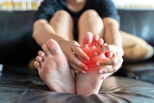 Foot Pain, Asian Woman Feeling Pain In Her Foot At Home, Female Suffering From Feet Ache Use Hand Massage Relax Muscle From Soles In Home Interior.